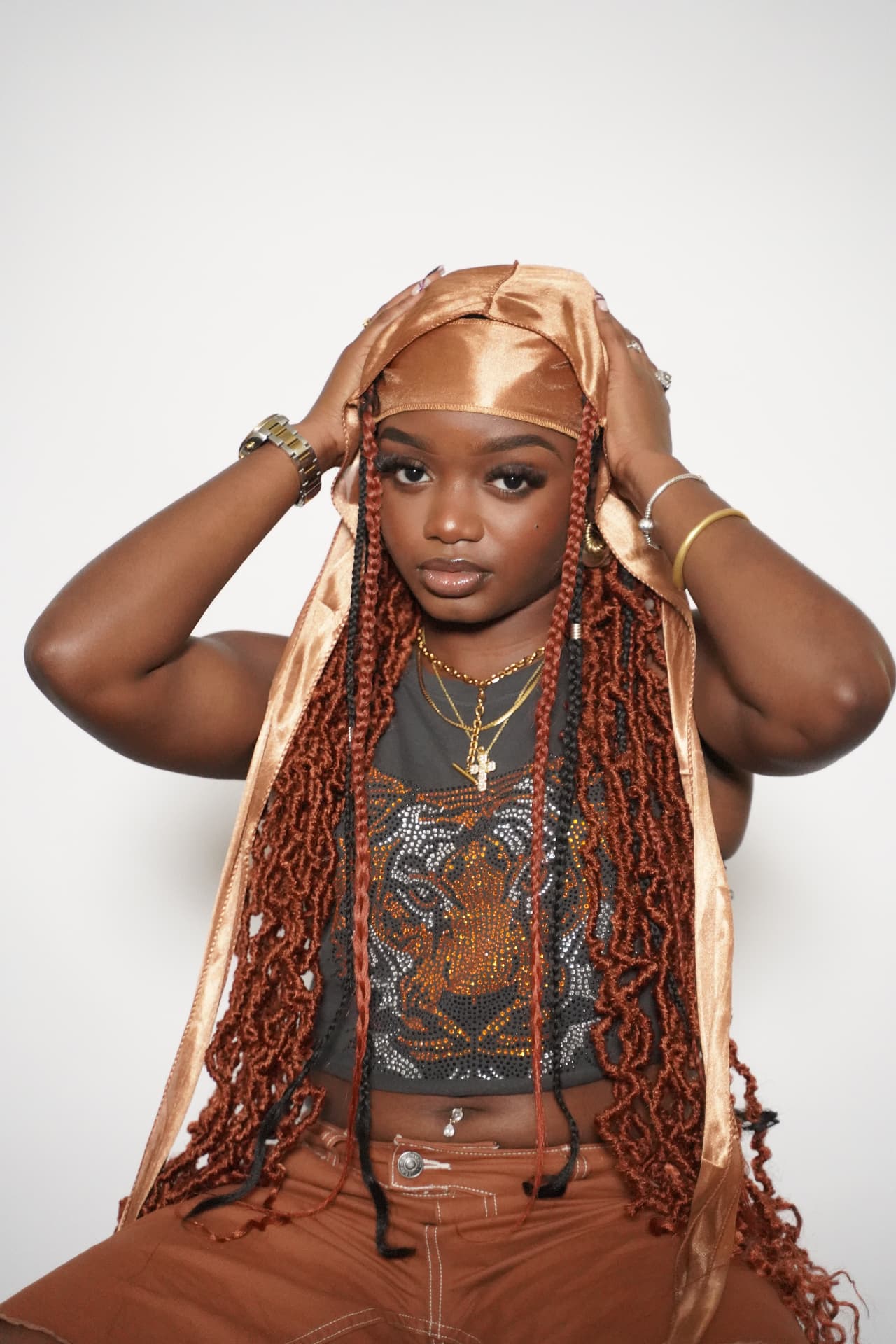 Model with long copper locs wearing the brown Elite Wrap, hands raised to the flap